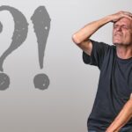 Persona stanca seduta alla scrivania con documenti medici e un computer.