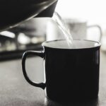 Tazza di acqua calda fumante su un tavolo, simbolo dei benefici per la salute al mattino.